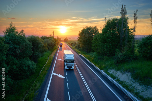 Obraz na płótnie White truck and red one driving on the highway in a rural landscape at sunset. View from above. w salonie