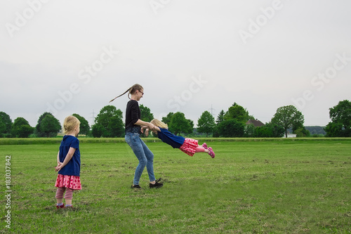 children fun running around the green field. two girls play with their older sister