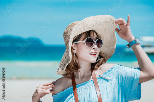 Young Asian woman wearing Hawaiian with hat and sunglasses is happy when they go to the beach for a holiday.