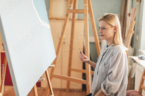Beautiful blonde woman artist drawing with a brush and pain in her art studio