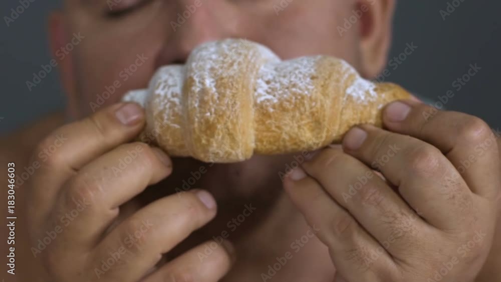 Closeup of overweight man enjoying a croissant, binge eating as mental problem Closeup of overweight man enjoying a croissant, binge eating as mental problem