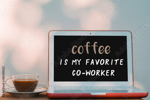Laptop computer with coffee quote - coffee is my favorite coworker and a cup of coffee on wooden desk. wall bokeh background for digital marketing and social media.