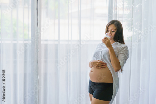 Beautiful pregnant woman standing and drink milk at living room. concept of pregnancy, family and lover relation. Free Download Beautiful pregnant woman standing and drink milk at living room. concept of pregnancy, family and lover relation. - GFXLoad