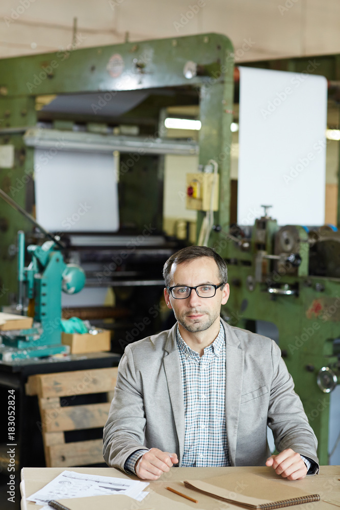 Young factory worker in casualwear sitting by table in industrial workshop Young factory worker in casualwear sitting by table in industrial workshop