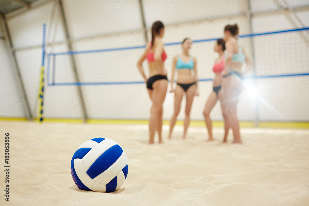 Volley ball on sand field on background of four young participants having break