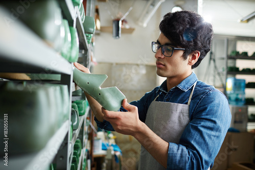 Bilde på lerret Young shoemaker taking one of footwear workpieces from shelf