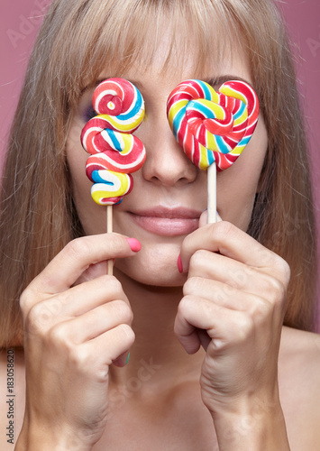 Beauty portrait of young blonde woman on pink background. Female with candy lollipop on stick in hands. photo