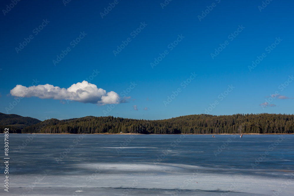 Winter landscape. Fishermen on frozen lake water, pine forest. Bulgaria, Rhodopes mountains, Shiroka Polyana lake.