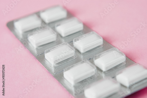 Close up of pile of white chewable antacid acid reducer tablets against heartburn and sour stomach in blister packaging on light pastel pink background photo