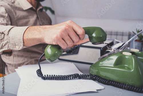 Man in vintage office uses green rotary telephone photo