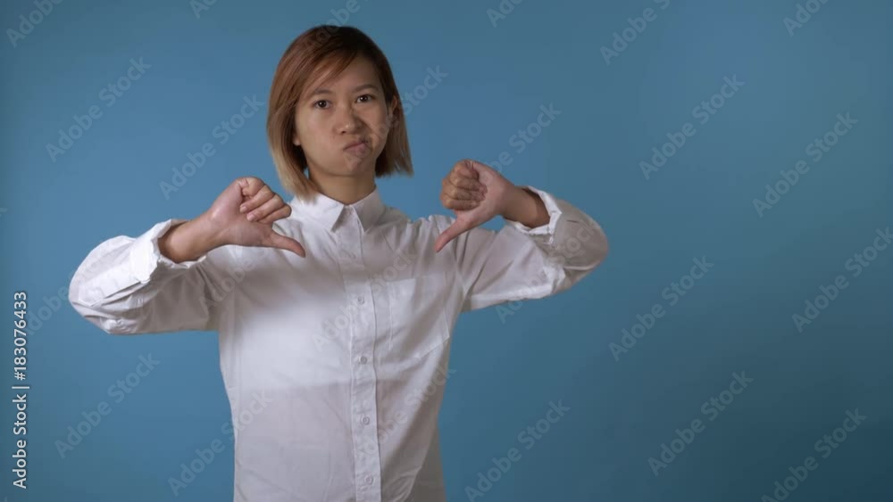 portrait young asian female posing showing hands gesture thumbs down on blue background in studio. attractive korean woman with blond hair wearing white casual shirt looking at the camera portrait young asian female posing showing hands gesture thumbs down on blue background in studio. attractive korean woman with blond hair wearing white casual shirt looking at the camera