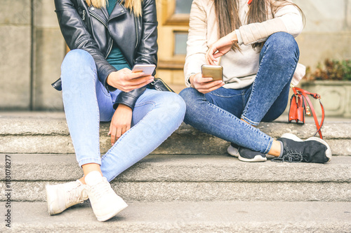 Young women using mobile phone while sitting on stairs of an urban area - Young generation addicted to new smart phones electronic devices - Concept of Social, technology, lifestyle