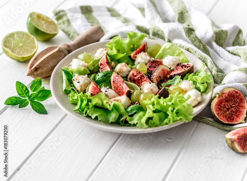 Salad with figs, mozzarella and grapes on a white wooden background.