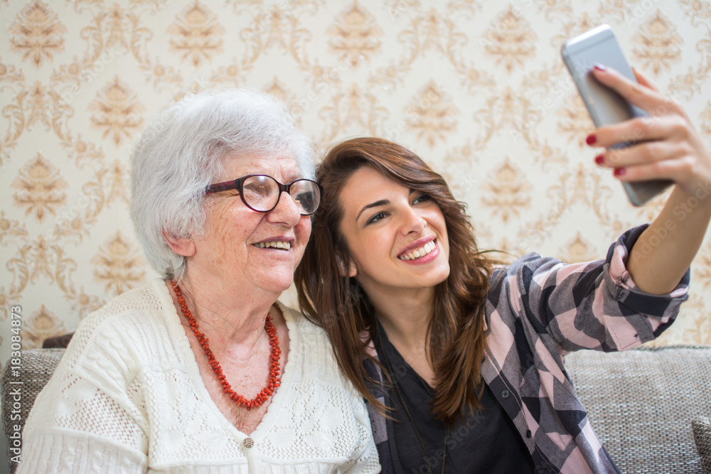 Smiling grandmother and granddaughter taking selfie photo on smart phone.