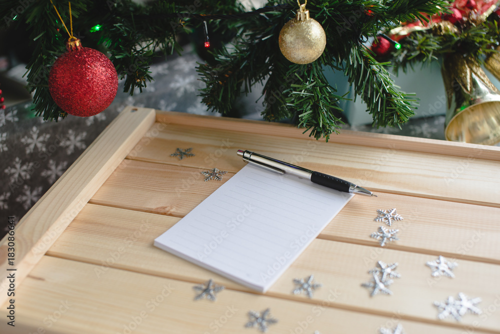 Fototapeta premium Wish list with a pen on the wooden box next to xmas tree. Christmas