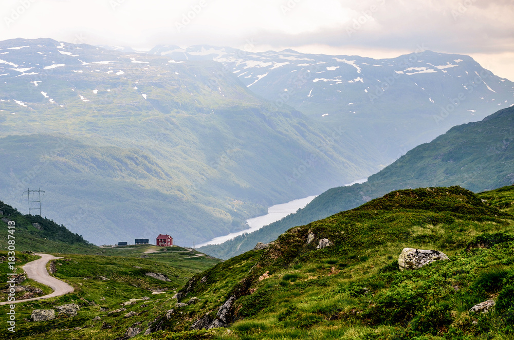 A small red house on the horizon above the deep and narrow fjord in Norway, Europe