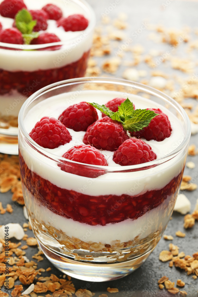 Dessert with raspberries and granola in glasses on grey wooden table Dessert with raspberries and granola in glasses on grey wooden table