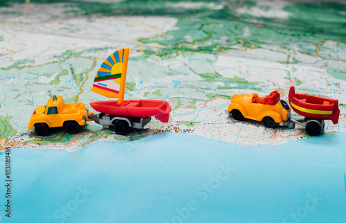 Two toy car carrying a boat and a sailboat. Two trailer driving on a topographic map