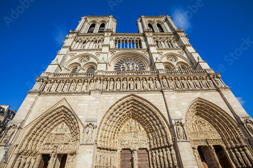 Details close up bottom view of French Gothic architecture of Notre Dame cathedral of Paris, France. Sunny blue cloudy sky. Our Lady of Paris church. Central main facade.