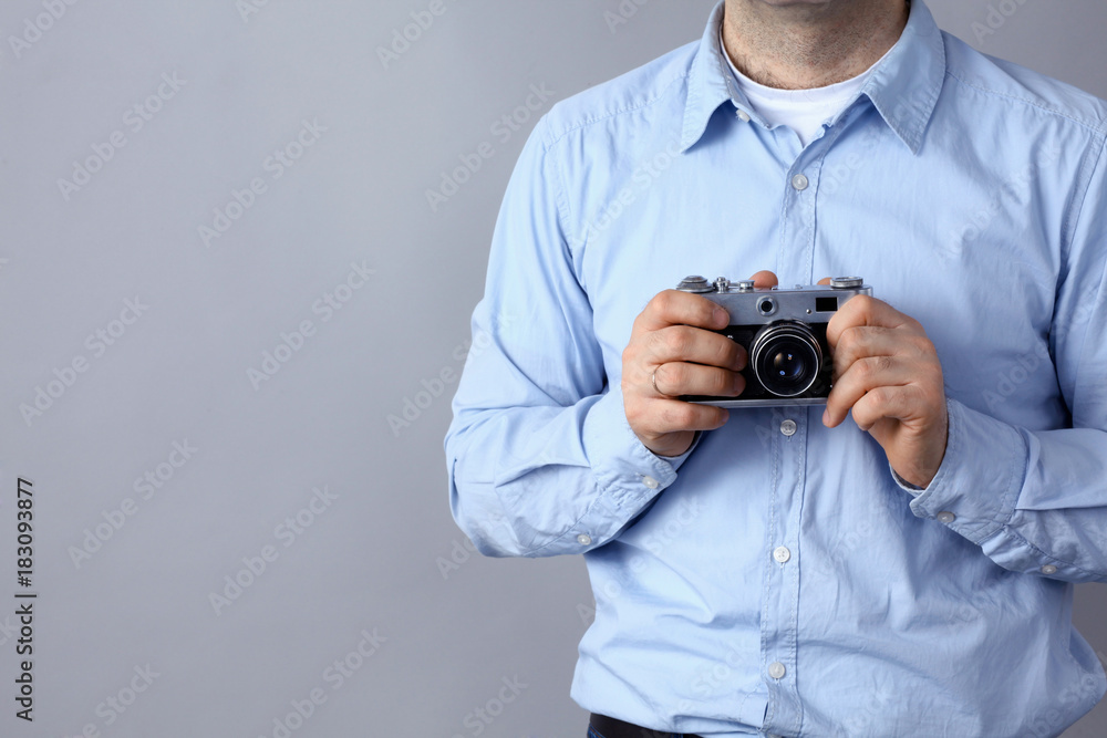 Young man holding a camera standing on gray background Young man holding a camera standing on gray background
