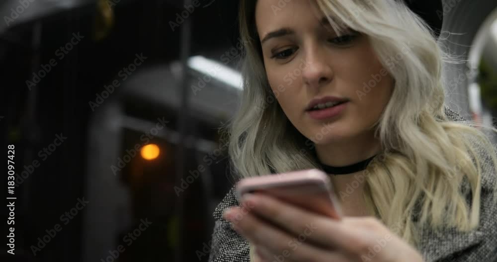 Close-up portrait of a smiling cute girl in black hat, browsing and typing message on her phone while travelling on the public transport. Close-up portrait of a smiling cute girl in black hat, browsing and typing message on her phone while travelling on the public transport.