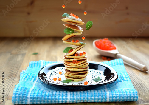 Flying pancakes, red caviar and basil leaves. Levitating food on a wooden background