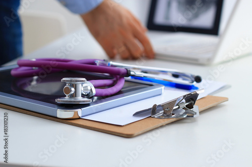 Male doctor using a laptop, sitting at his desk with medical stethoscope