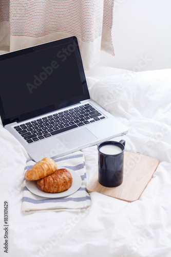 milk, laptop and croissants to show a business breakfast on the bed table in morning