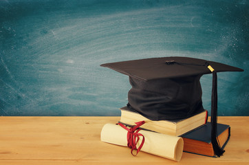 Image of graduation black hat over old books next to graduation on wooden desk. Education and back to school concept.