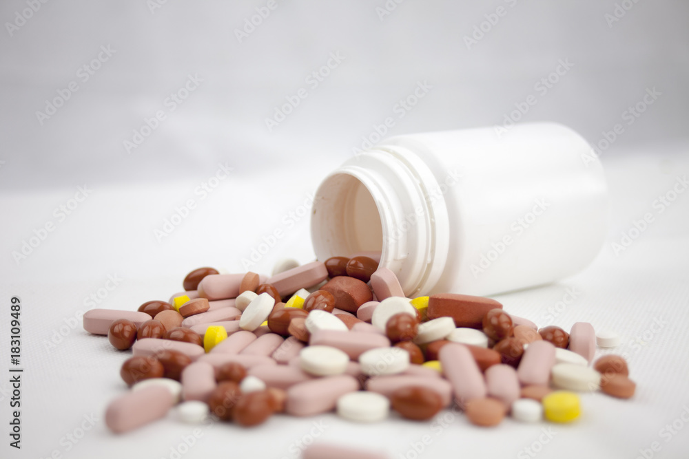 Colorful pills laying on the white background with empty bottles