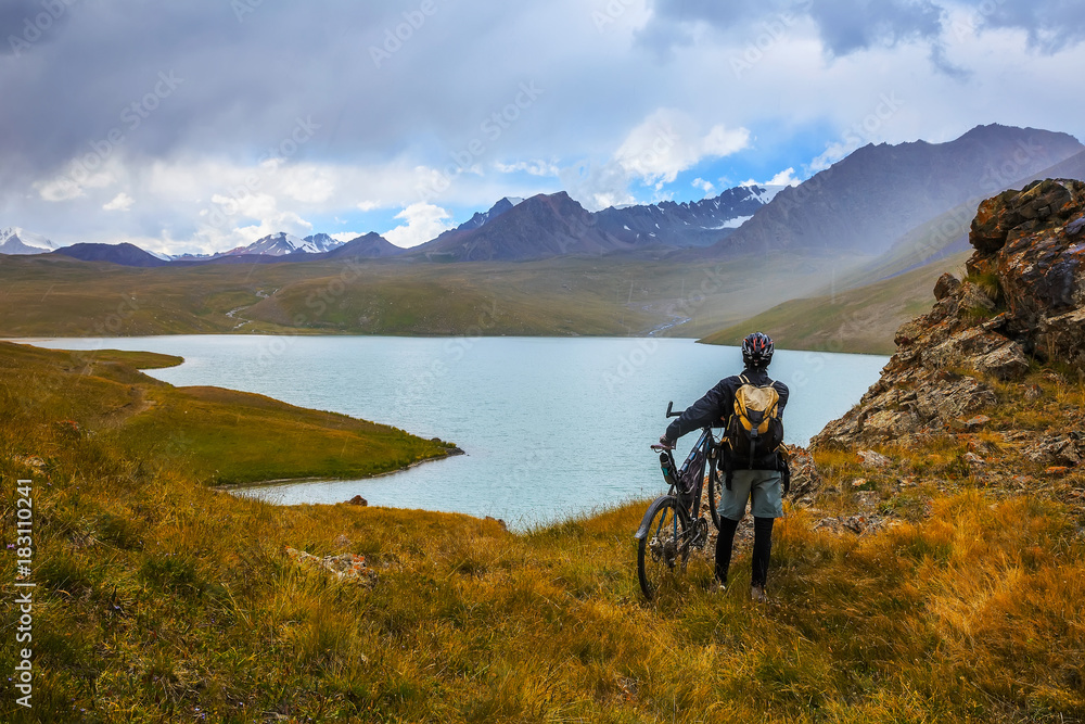 A guy with a bicycle on the background of high mountains. Lake Teshik-Kul.  Kyrgyzstan.