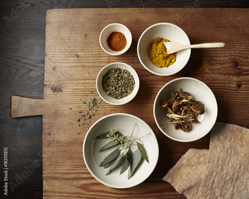 Spices, mushrooms and leaves in white bowls on a rustic wooden cutting board