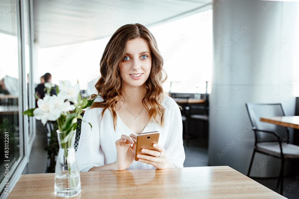 the nice business lady speaks by smartphone in street cafe. the girl has blue eyes and a fair hair, she is dressed in a white blouse the nice business lady speaks by smartphone in street cafe. the girl has blue eyes and a fair hair, she is dressed in a white blouse