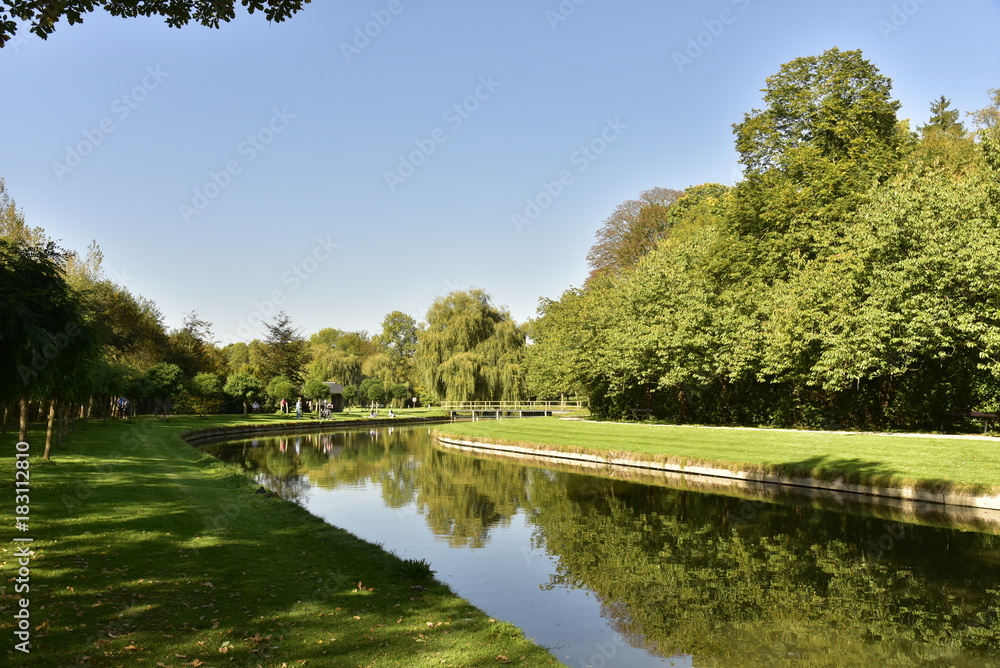 Courbe du chenal principal et son effet miroir reliant le petit et le grand étang dans un cadre verdoyant au Vrijbroekpark à Malines Courbe du chenal principal et son effet miroir reliant le petit et le grand étang dans un cadre verdoyant au Vrijbroekpark à Malines