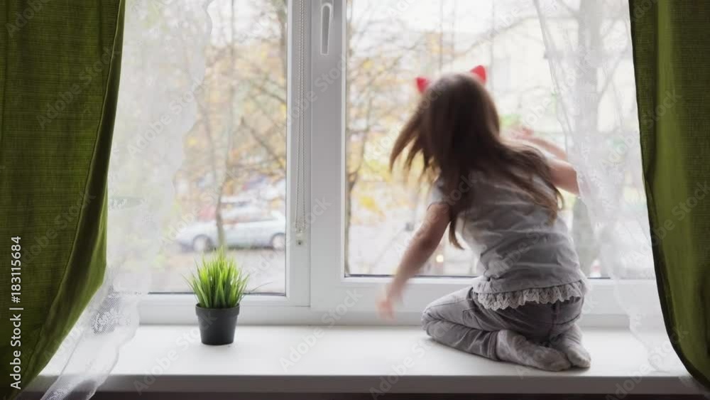 Little girl climbed onto the windowsill and looking out the window Little girl climbed onto the windowsill and looking out the window