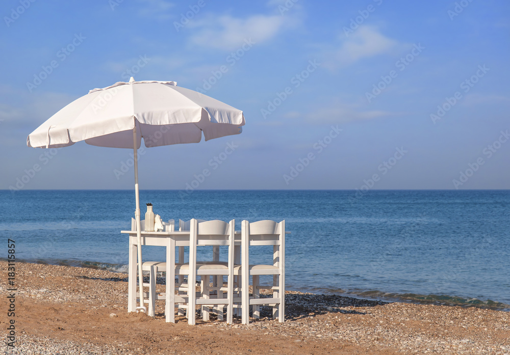 Fototapeta premium White wooden table on beach with blue sea with four chair and umbrella