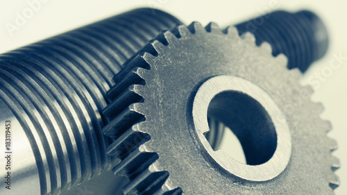 Close-up of steel gearwheel and shaft with thread. Abstract engineering background with cogwheel and bolt.