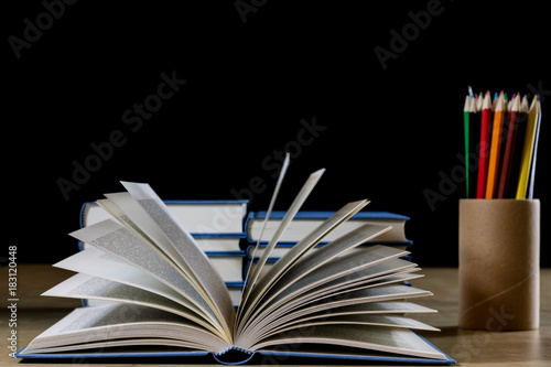 Heap of books reading on a wooden table. Beside lies and Colourful pencils. Black background.