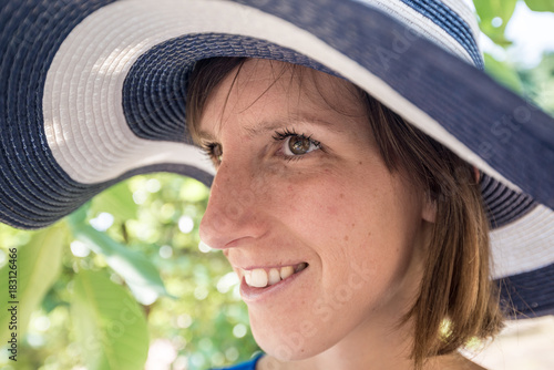 Side view of a woman standing outdoors in a wide brimmed blue and white sunhat photo