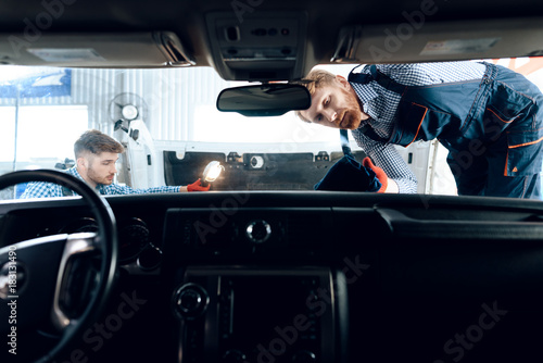 Father and son work at the auto service. Two mechanics work with the details of the car.