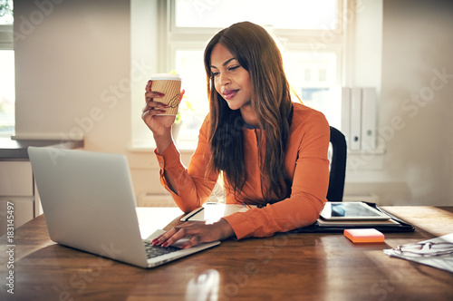 Smiling young entrepreneur working in her home office drinking c photo