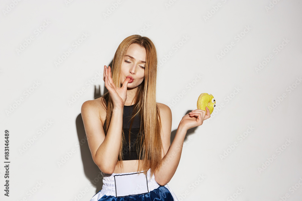 Close up of attractive young female model with yellow donut in hand, holding finger in mouth with closed eyes and big satisfaction. Close up of attractive young female model with yellow donut in hand, holding finger in mouth with closed eyes and big satisfaction.