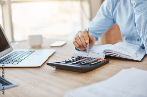 Close up detail of professional serious accountant sitting in light office, checking company finance profits on calculator, writing down results in notebook. Business concept.