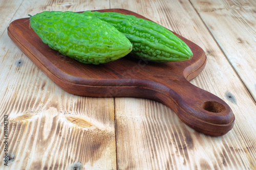 Fresh bitter melon or bitter gourd (Momordica charantia) on wooden cutting boards over pine wood grain