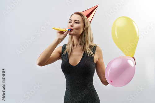 Portrait of a cheerful young stylish women girls posing for a portrait on isolated background with ceremonial attributes (in the hood for a party, pipe the whistle and balloons)