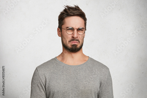 Negative human expressions and attitude. Angry dissatisfied male has disgusting expression as sees something not appealing, frowns face, isolated over white concrete background. Distaste and dislike