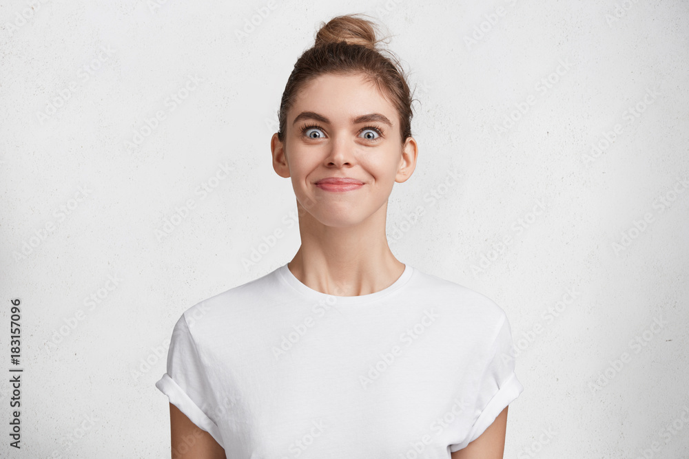 Cheerful female model with happy expression and charming appearance, has dark hair tired in knot, glad to meet handsome guy, isolated over white background. Emotional young beautiful woman indoor Cheerful female model with happy expression and charming appearance, has dark hair tired in knot, glad to meet handsome guy, isolated over white background. Emotional young beautiful woman indoor