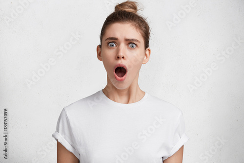 Photo of surprised shocked woman keeps mouth widely opened, looks with dissatisfied expression as finds about her big failure in preparing report, should do everything from begining. Omg concept photo