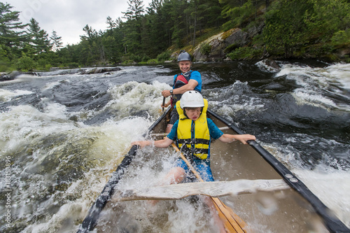 Young boy paddling whitewater in a canoe