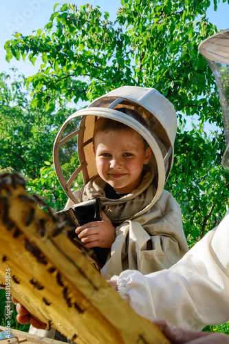 A boy wearing a protective suit in an apiary near a hive with bees. © kosolovskyy